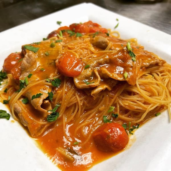 Spaghetti with tomato sauce, cherry tomatoes, thinly sliced meat, and fresh parsley on a white plate.