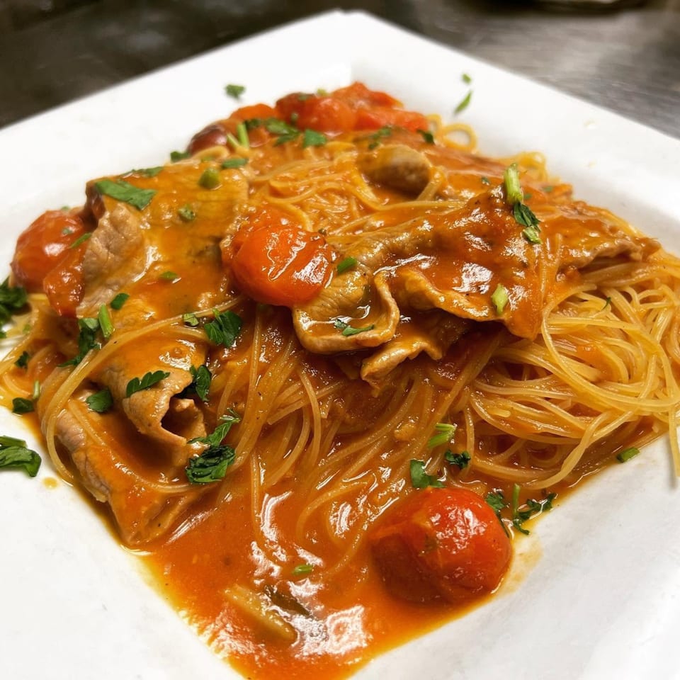 Spaghetti with tomato sauce, cherry tomatoes, thinly sliced meat, and fresh parsley on a white plate.