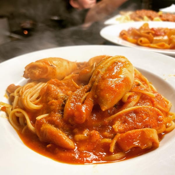 Steaming spaghetti with squid and rich red tomato sauce in a white bowl.