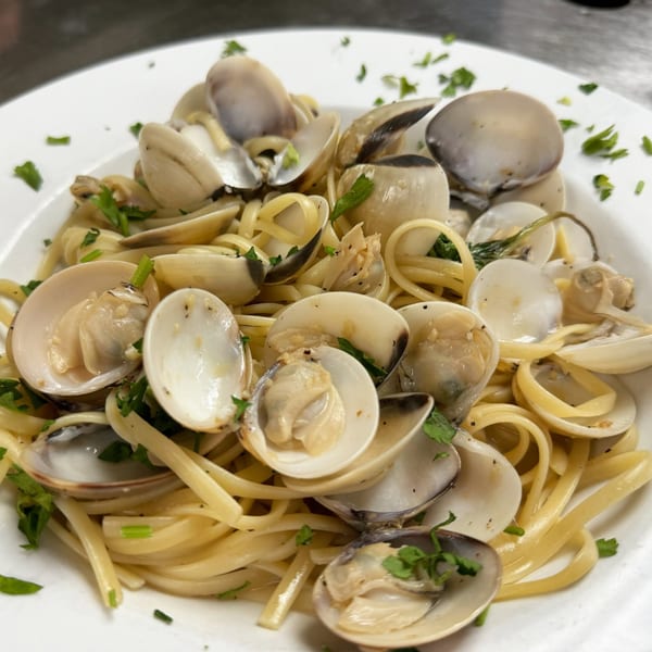 Close-up of linguine pasta with clams and fresh parsley on a white plate.