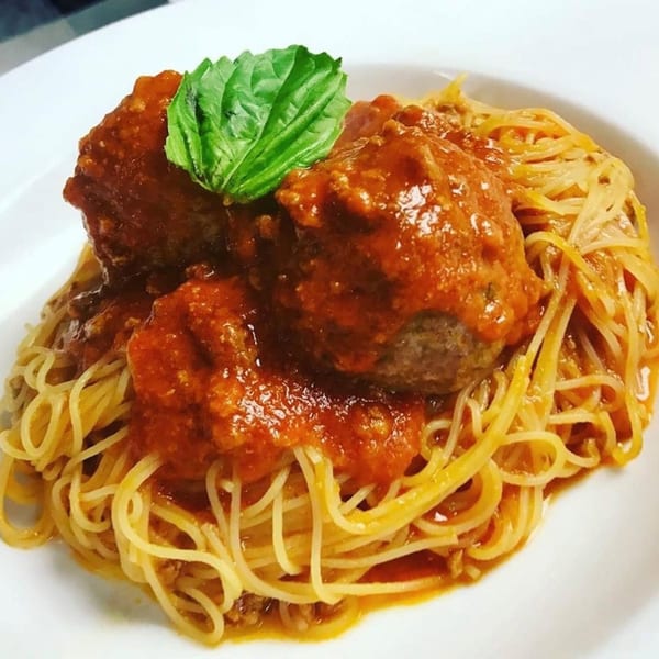 Spaghetti with two large meatballs covered in red sauce and garnished with a fresh basil leaf.