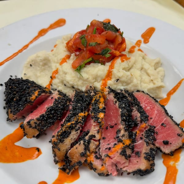 Seared tuna with black sesame crust, mashed potatoes, tomato relish, and orange sauce on a white plate.