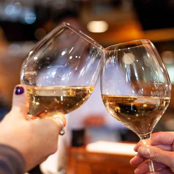 Two hands clinking wine glasses filled with white wine, celebrating in a restaurant.